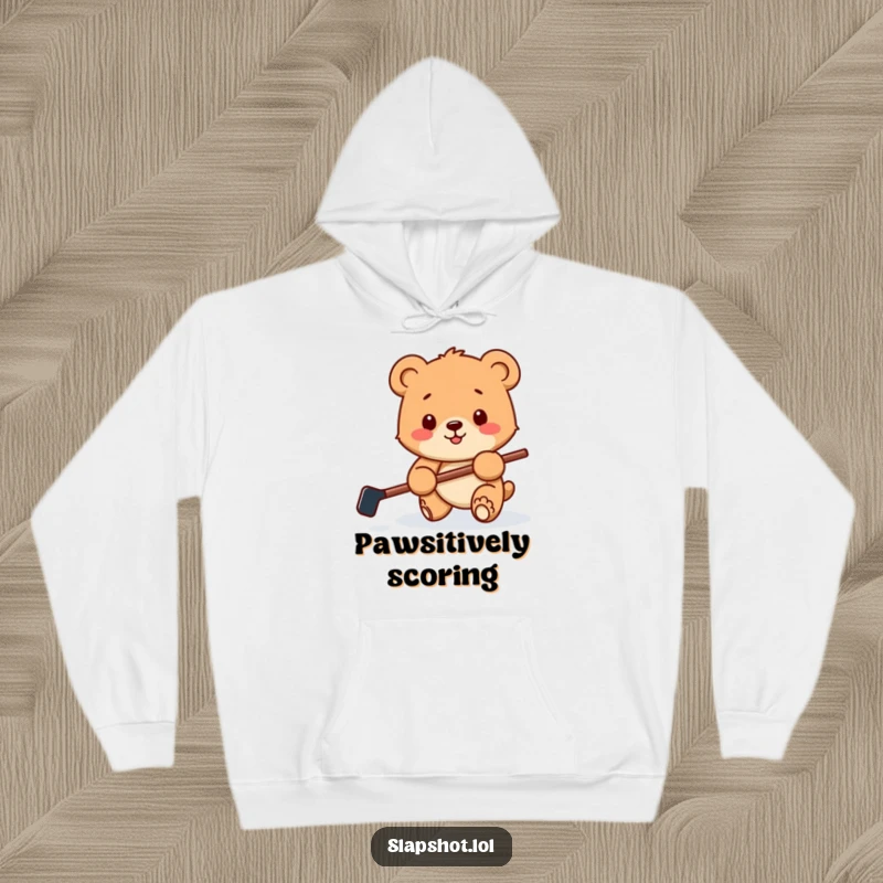 Funny hoodie featuring a happy bear cub with a miniature hockey stick, playfully batting a puck, offering cozy sports fun.